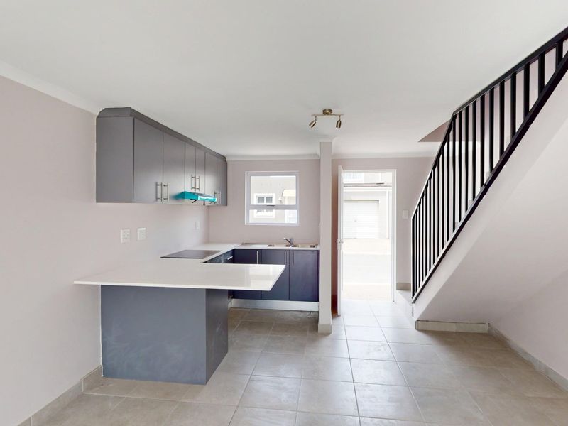 Open-plan kitchen featuring modern grey cabinetry, stone countertops, and an electric hob, adjacent to a staircase with a metal balustrade.