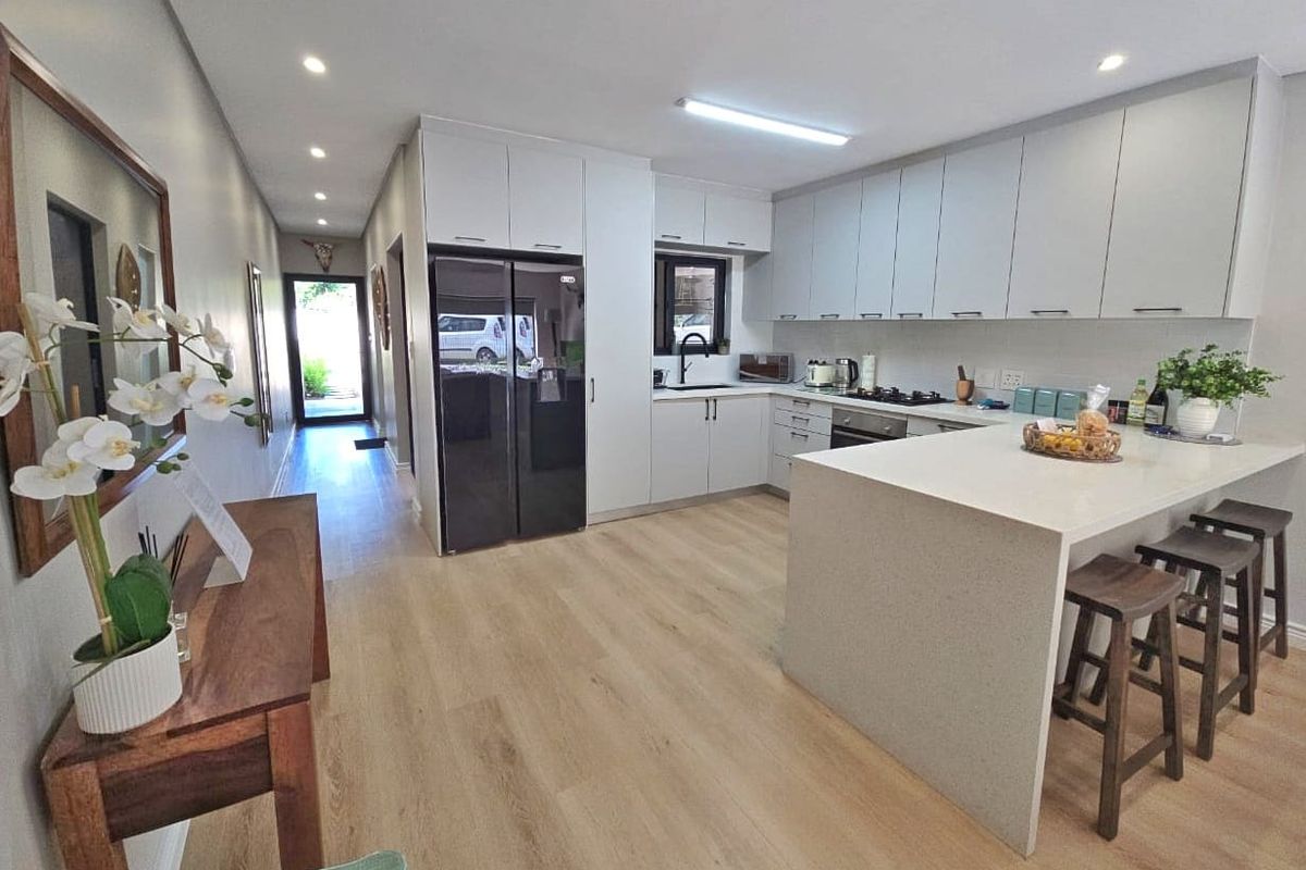 Modern open-plan kitchen featuring sleek cabinetry, stone countertops, integrated appliances, and light laminate flooring, flowing seamlessly into the hallway.
