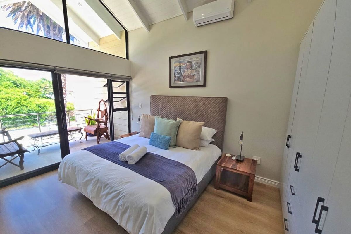 Spacious bedroom featuring vaulted ceilings, laminate flooring, built-in cupboards, and large sliding glass doors opening to a private balcony.