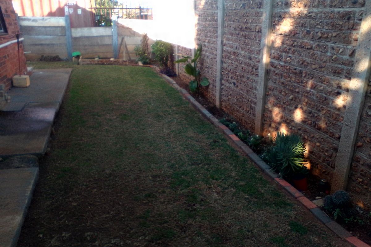 A private rear garden area featuring a lawn, concrete paving, and a precast concrete boundary wall.