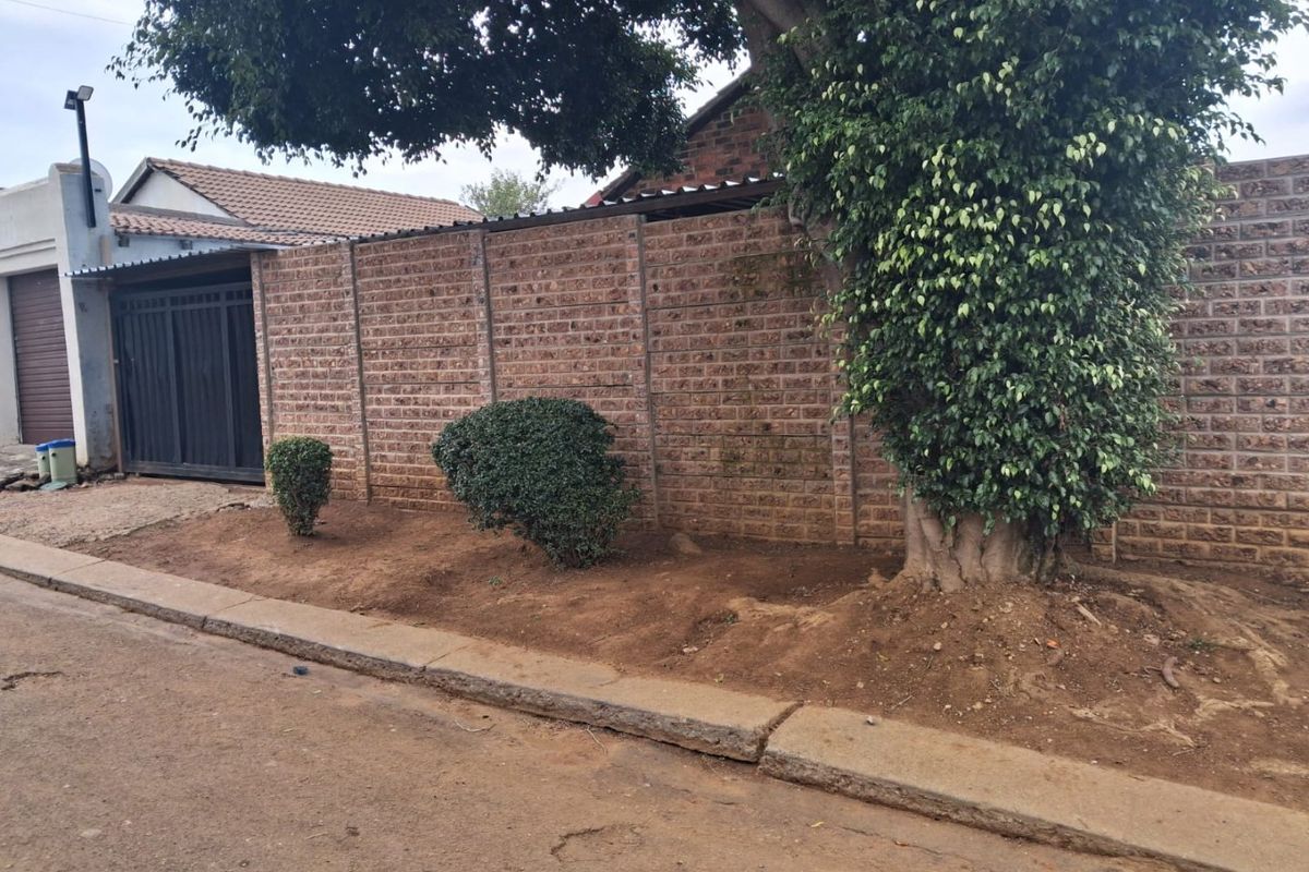 Front exterior view showing a brick boundary wall, metal garage door, and concrete kerb along the street frontage.