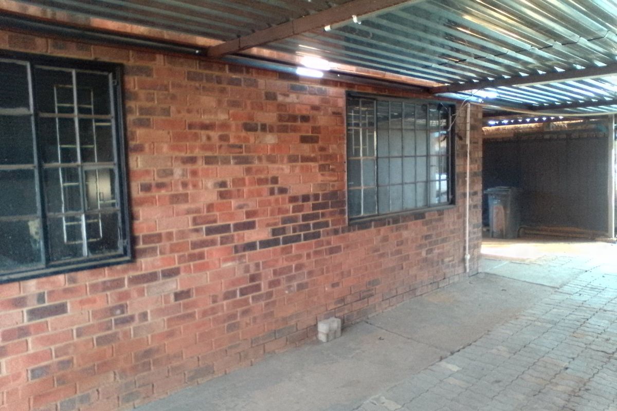 A covered outdoor area featuring a brick facade, corrugated metal roofing, and secure steel-framed windows, providing a functional utility or parking space.