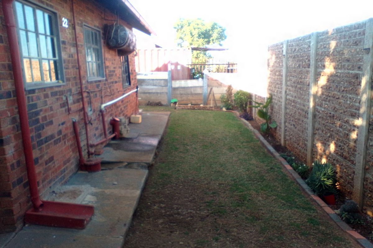 A side view of the property featuring a brick exterior, concrete pathway, and a private garden area enclosed by a precast concrete boundary wall.