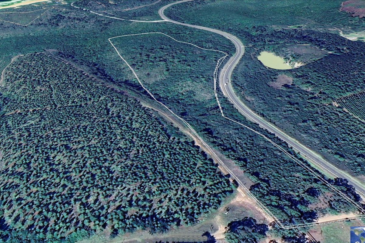 Aerial view of a large rural farm property featuring natural vegetation, bordering a main road, with marked boundary lines.