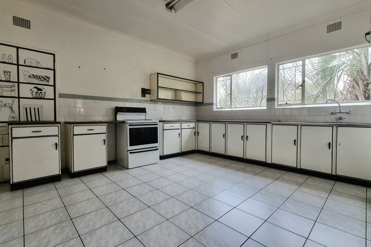 A spacious, empty kitchen featuring original built-in cabinetry, tiled flooring, and a freestanding stove, offering a blank canvas for modern renovation.