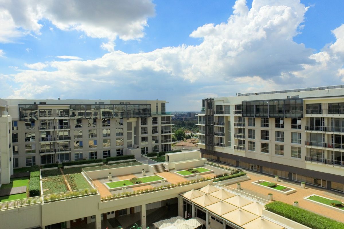 An elevated aerial view of a modern apartment complex featuring landscaped rooftop gardens, paved communal areas, and contemporary building facades.