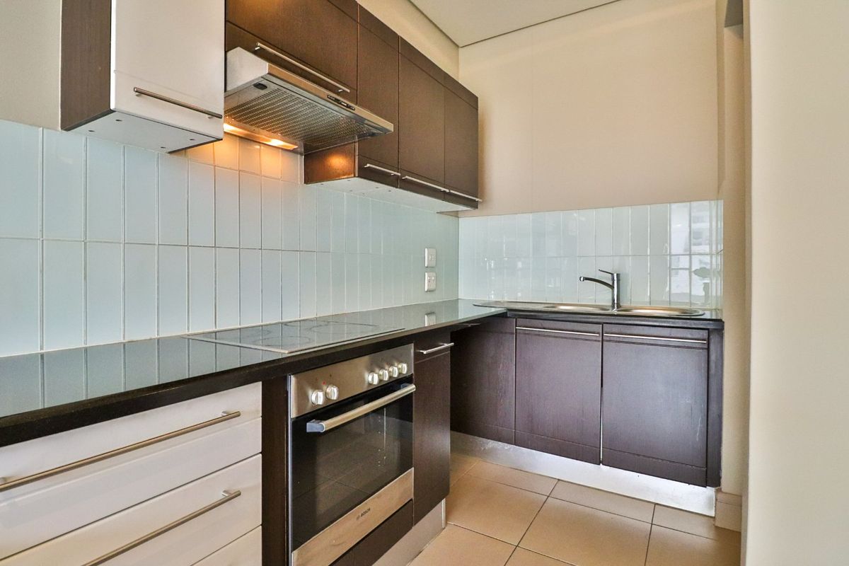 Modern kitchen featuring dark wood cabinetry, stone countertops, integrated electric hob, oven, extractor fan, and a clean tiled backsplash.