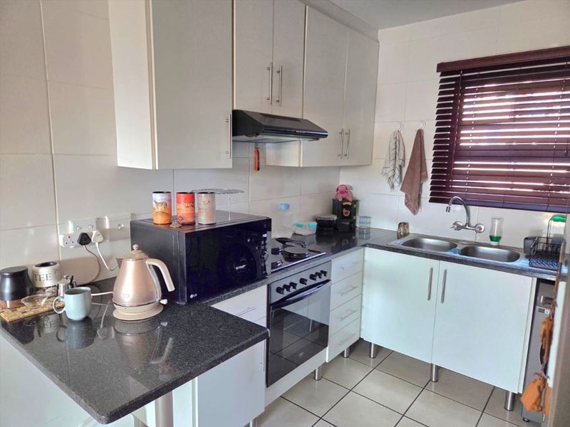 A functional kitchen featuring white cabinetry, granite countertops, a double basin sink, and built-in cooking appliances with tiled flooring.