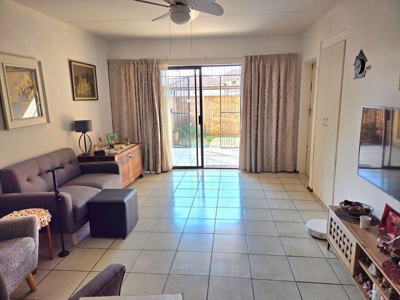 A bright living room featuring tiled flooring, a ceiling fan, and a sliding glass door providing direct access to the rear patio area.