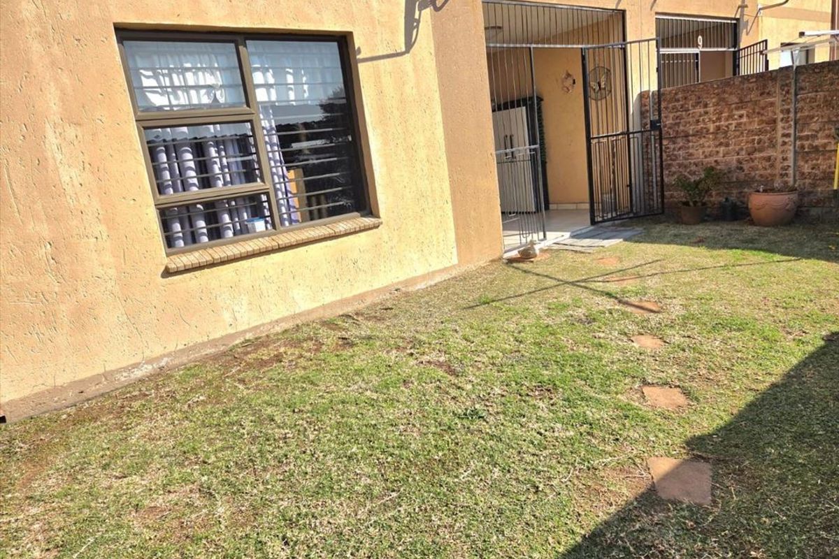 Rear exterior view of the townhouse featuring a small private garden, security gate, and brick boundary wall.