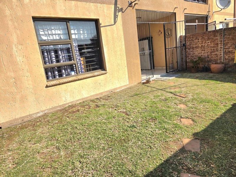 Rear exterior view of the townhouse featuring a small private garden, security gate, and brick boundary wall.