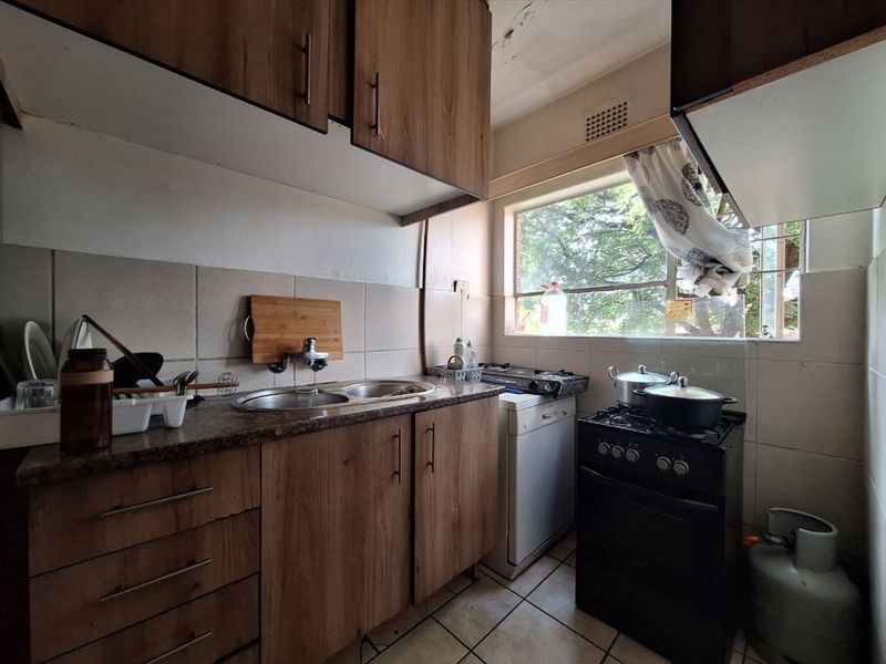 A compact kitchen featuring laminate cabinetry, granite countertops, and a tiled backsplash, currently showing signs of wear and ceiling damage.