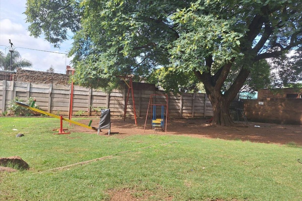 A spacious communal garden area featuring a large mature tree, lawn, and precast concrete boundary walling.