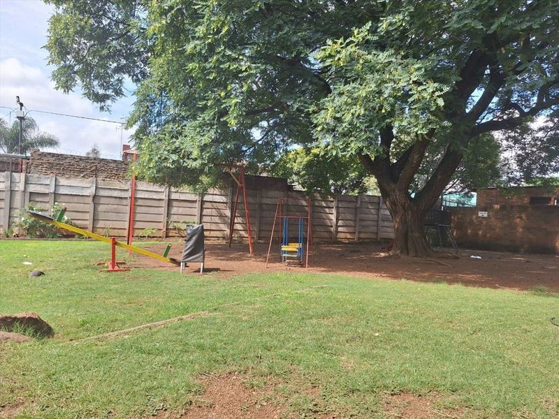 A spacious communal garden area featuring a large mature tree, lawn, and precast concrete boundary walling.