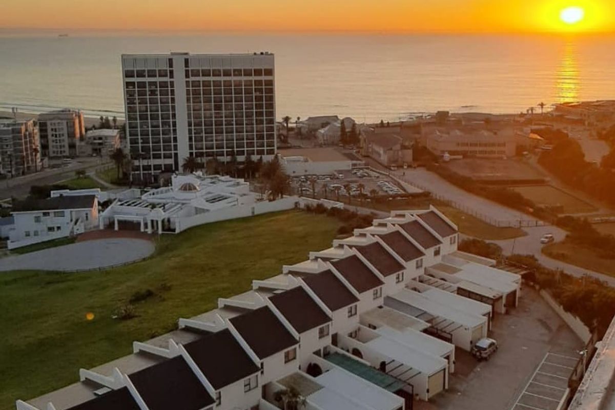 An elevated aerial view of a coastal residential complex at sunset, showcasing the surrounding neighborhood and proximity to the ocean.