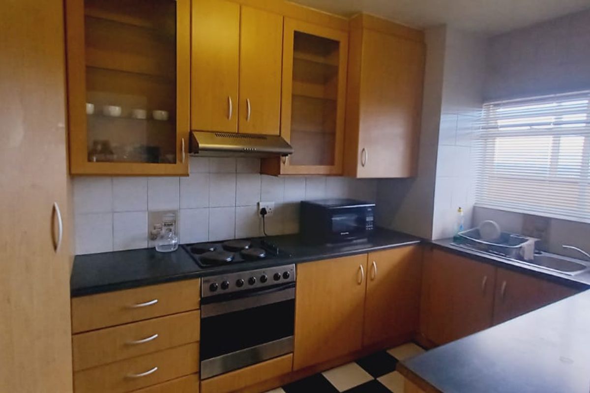 A functional kitchen featuring wooden cabinetry, an integrated electric stove with oven, extractor fan, and a double sink with tiled backsplash.