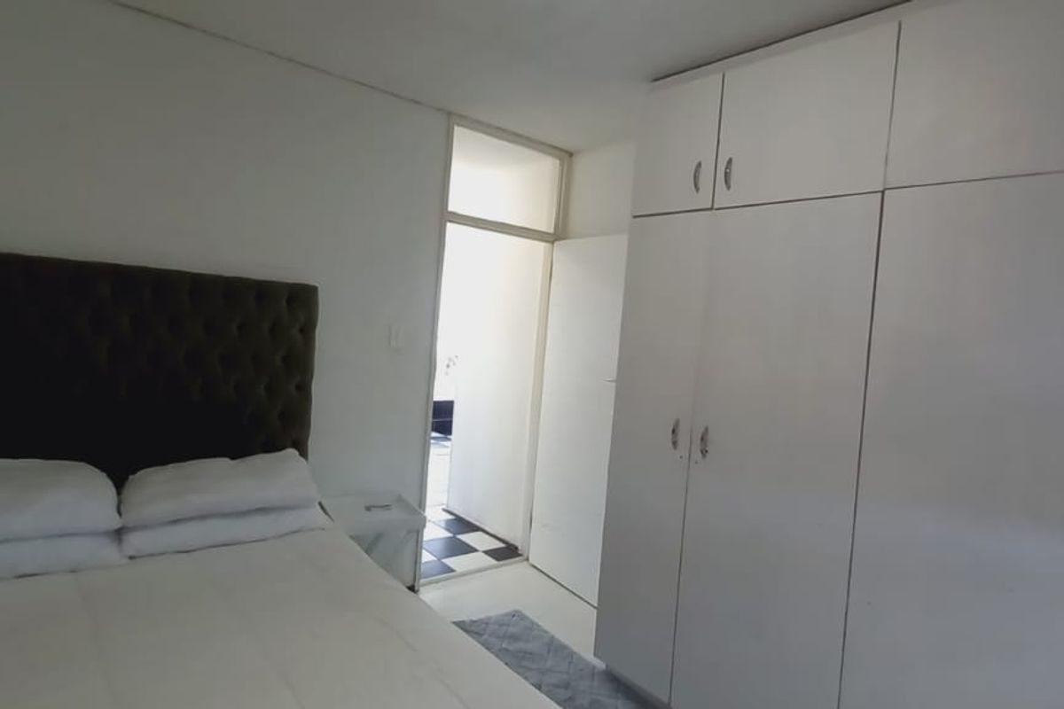 A bedroom featuring white built-in cupboards and access to an adjacent room with tiled flooring.
