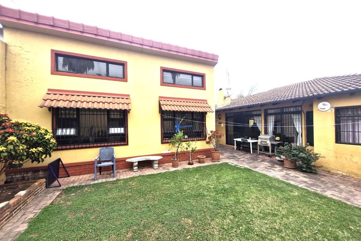 Rear view of the property featuring a paved patio area, lawn, and yellow exterior walls with security bars on the windows.