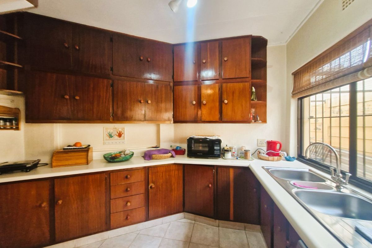 A functional kitchen featuring traditional wooden cabinetry, laminate countertops, and a double bowl stainless steel sink with a window view.
