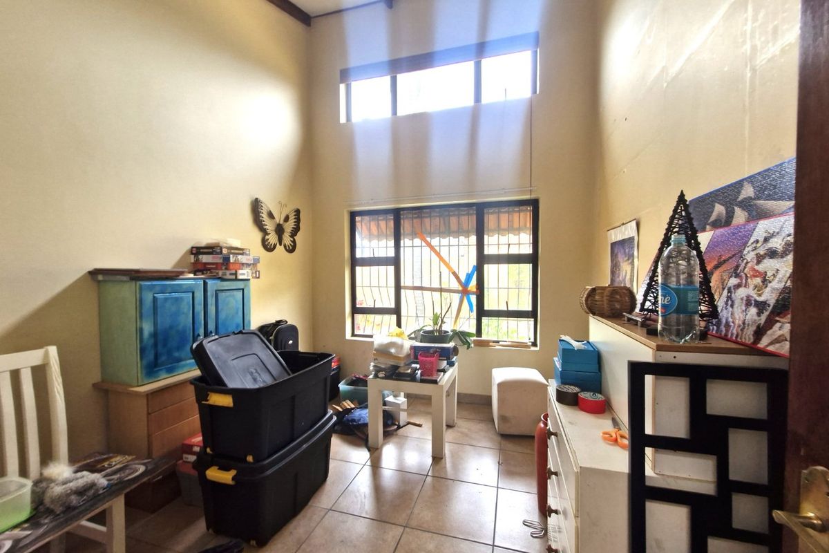 A bedroom featuring high ceilings with exposed timber beams, tiled flooring, and security-barred windows, offering a bright space with potential for modernization.