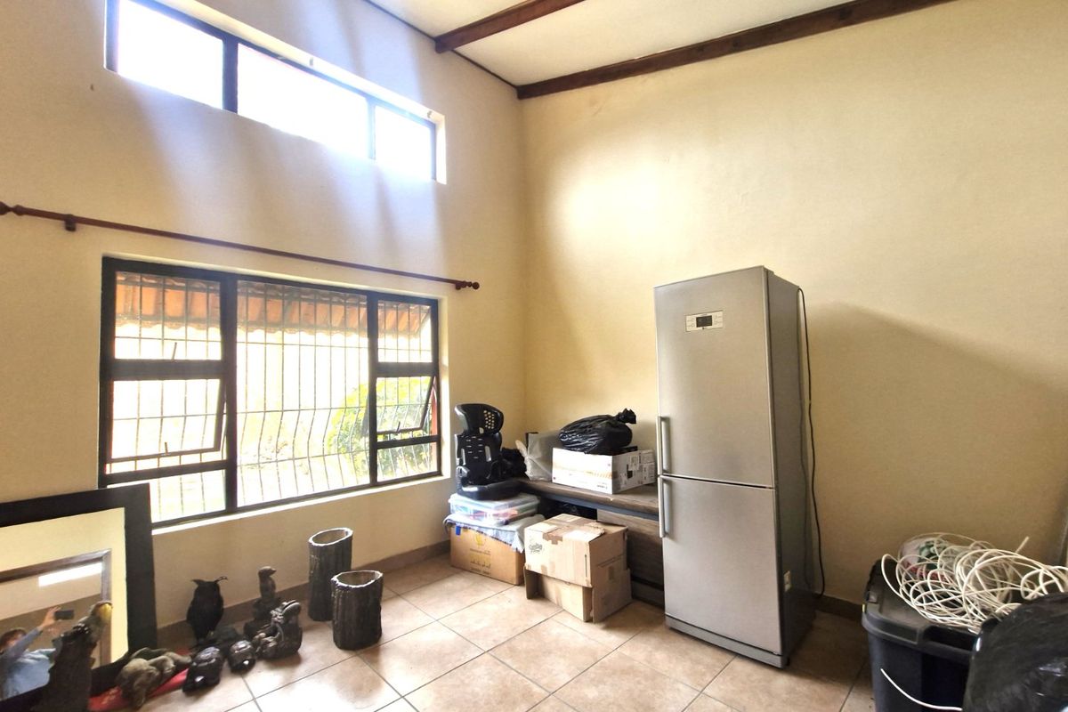 A living area featuring high ceilings with exposed timber beams, tiled flooring, and large windows with security bars, offering potential for modernization.