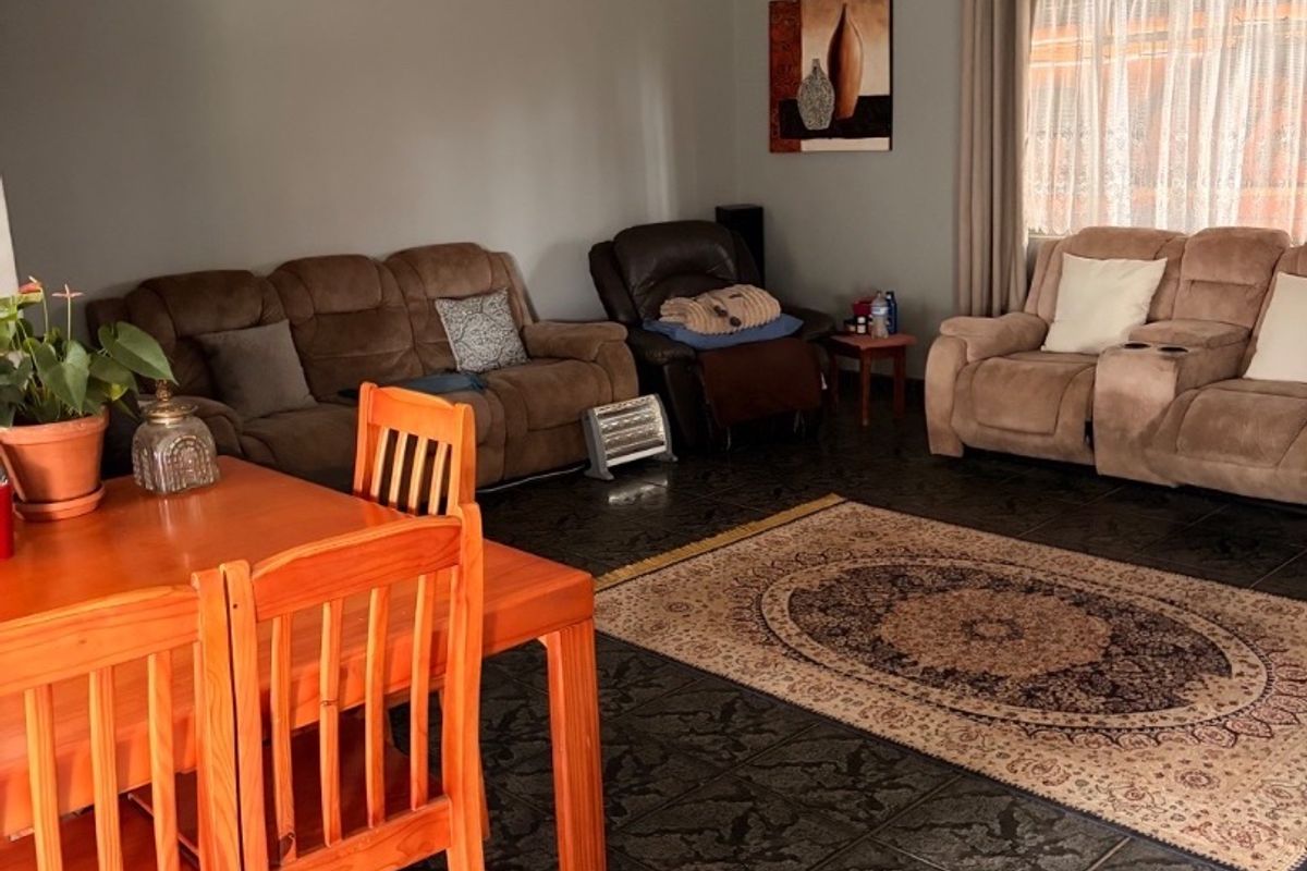 A spacious living area featuring dark patterned floor tiles, neutral wall tones, and a ceiling fan, providing a comfortable and functional family space.