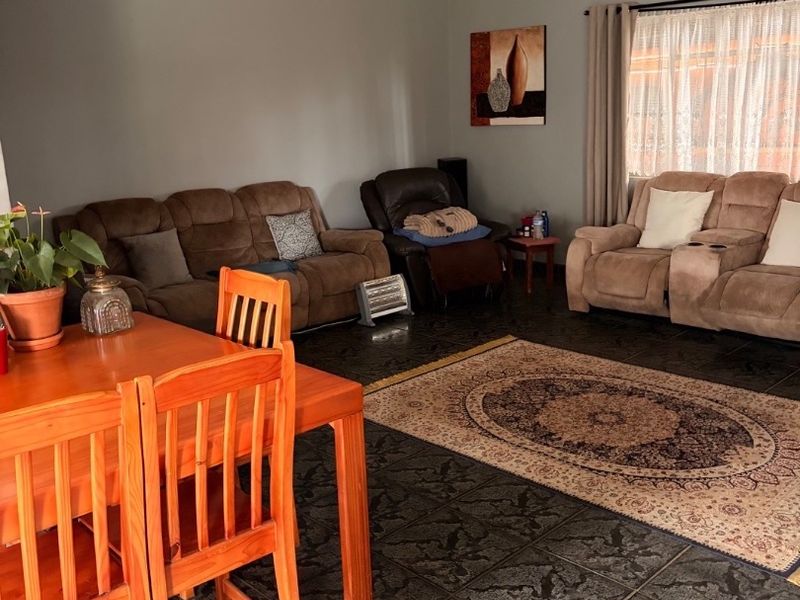 A spacious living area featuring dark patterned floor tiles, neutral wall tones, and a ceiling fan, providing a comfortable and functional family space.