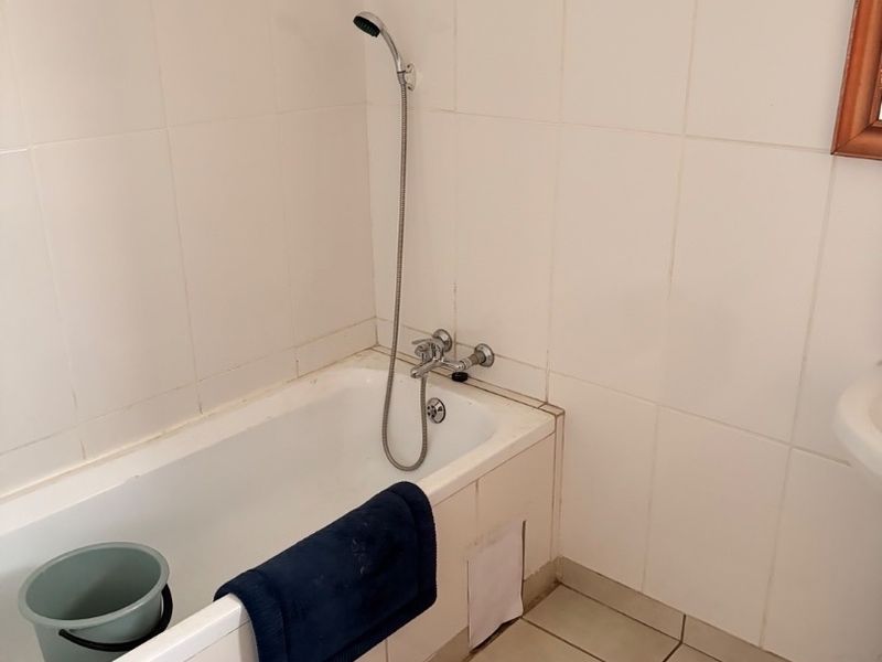 A functional bathroom featuring a standard bathtub with a handheld shower mixer, white wall tiling, and ceramic floor tiles.