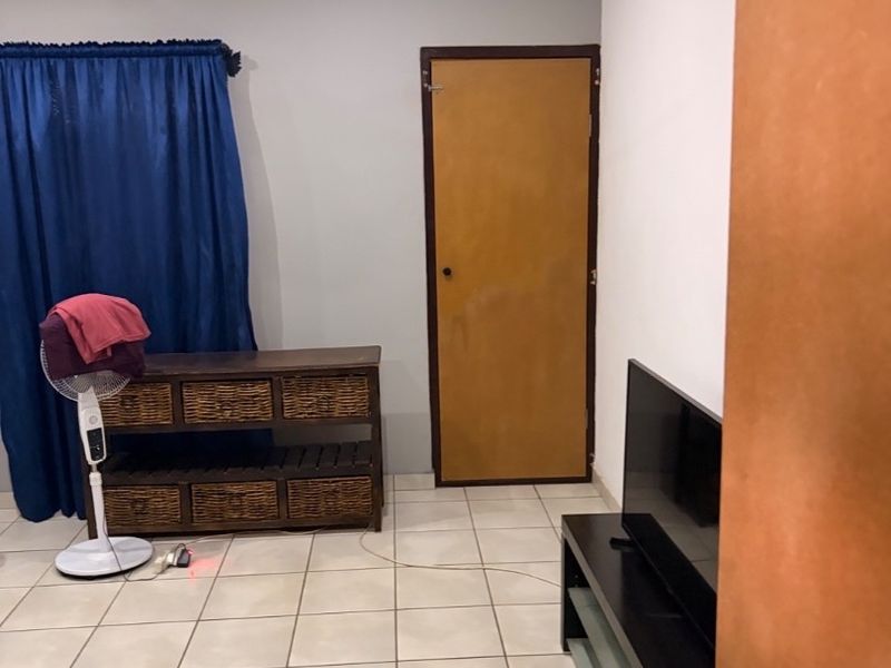 A functional living room featuring neutral tiled flooring, recessed lighting, and a standard internal door, offering a blank canvas for interior updates.