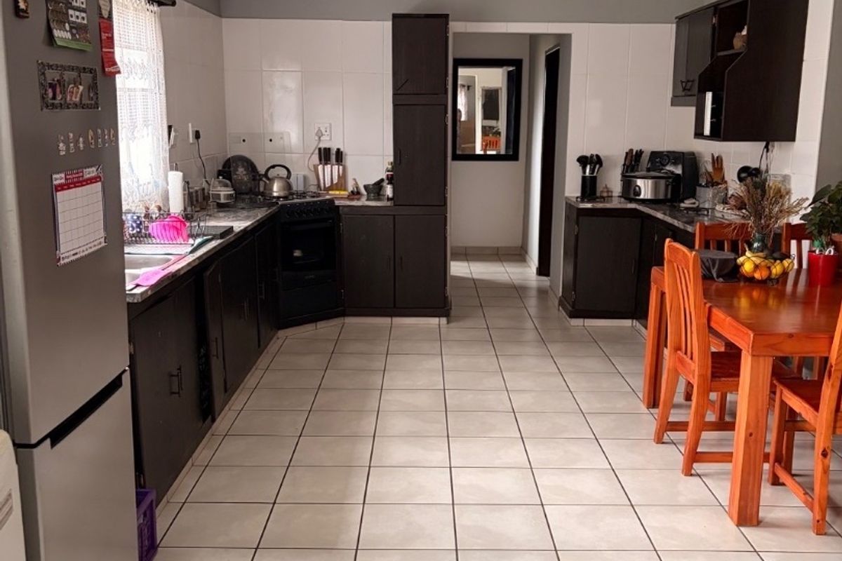 A functional kitchen featuring dark cabinetry, tiled flooring, a built-in oven and hob, and a tiled splashback, offering a practical layout for daily use.