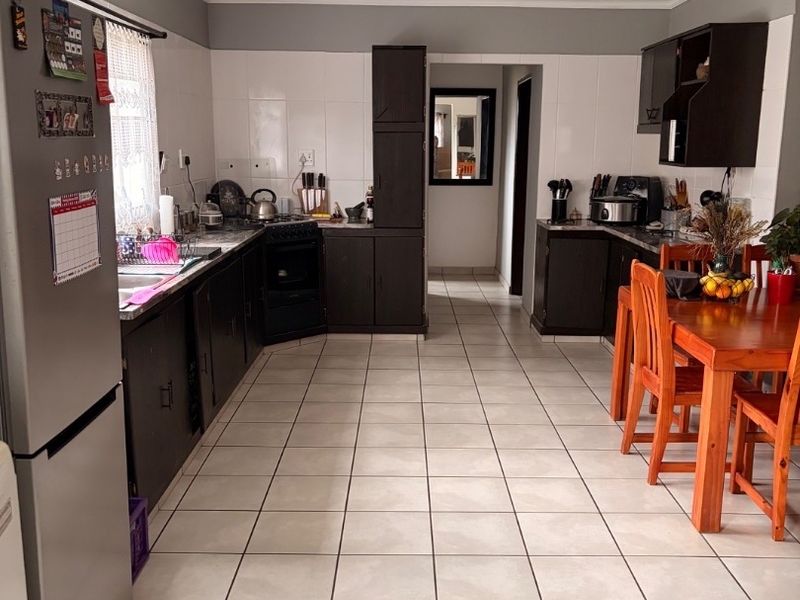 A functional kitchen featuring dark cabinetry, tiled flooring, a built-in oven and hob, and a tiled splashback, offering a practical layout for daily use.