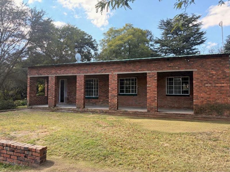A single-story face brick house featuring a covered front patio, security bars on windows, and a corrugated metal roof set in a garden.