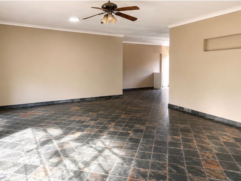 A spacious, empty living area featuring dark slate tile flooring, a ceiling fan, and a built-in wall niche, offering a neutral canvas for interior design.