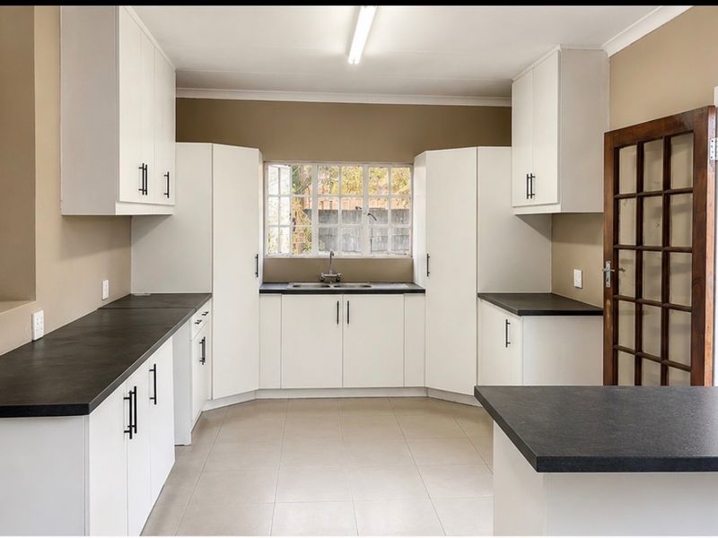 A clean, functional kitchen featuring white cabinetry, dark countertops, tiled flooring, and direct access to the garden through a timber-framed glass door.
