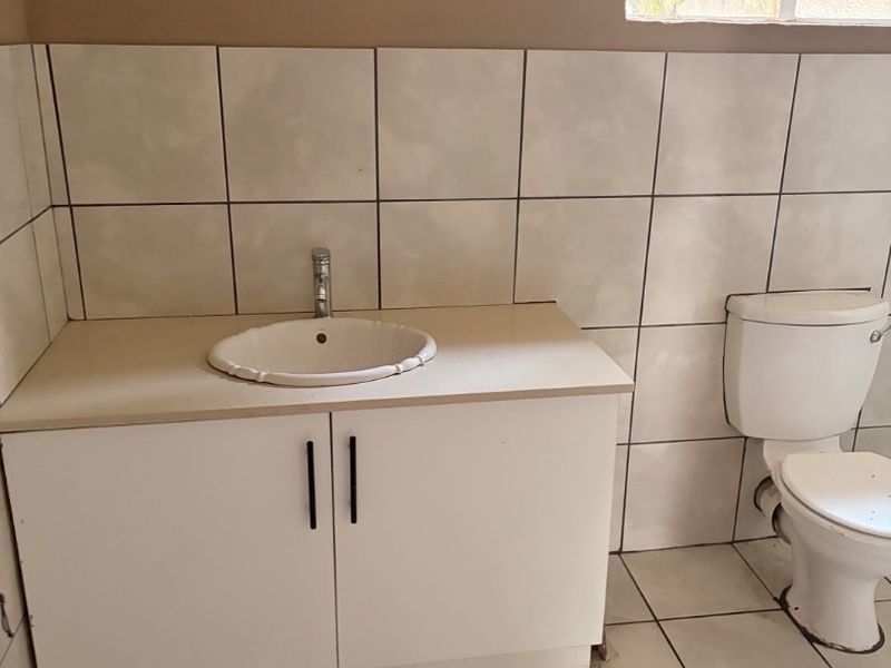 A functional bathroom featuring a vanity cabinet with basin, toilet, and tiled finishes throughout, offering potential for modernization.