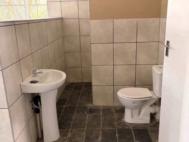 A functional bathroom featuring a pedestal basin, toilet, neutral wall tiling, and dark slate flooring.