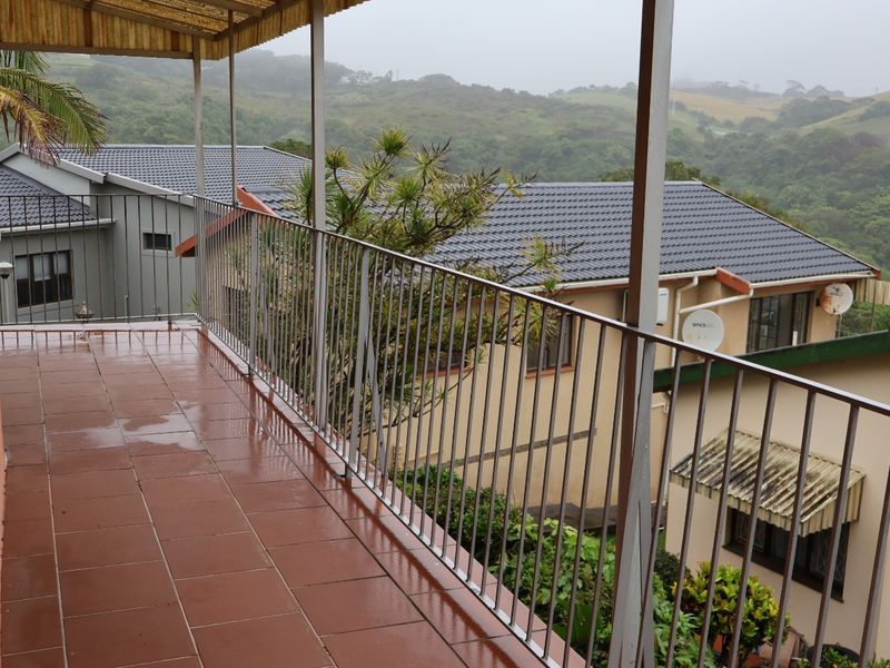 A covered balcony with tiled flooring and metal balustrades, offering elevated views of the surrounding residential area and landscape.