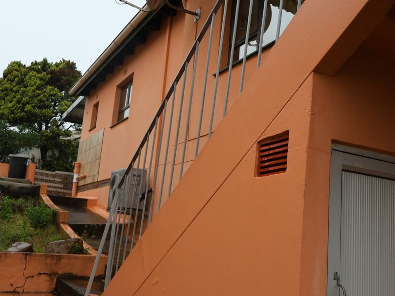Exterior view of the townhouse rear featuring an external staircase with metal railing, air conditioning unit, and concrete retaining walls.