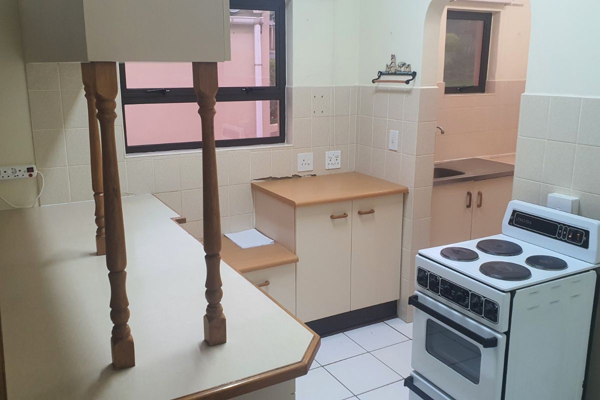 A dated kitchen featuring tiled flooring, laminate countertops, and a separate scullery area with a sink, offering potential for modern renovation.