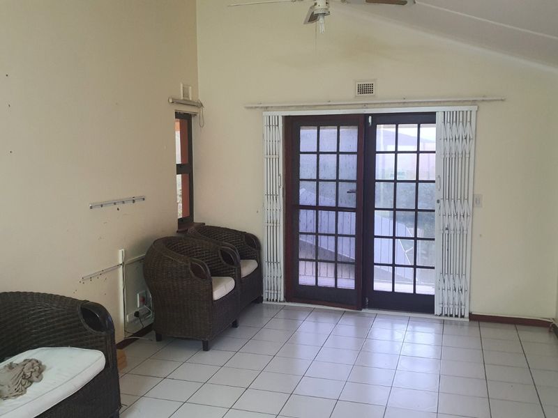 A living area featuring tiled flooring, a ceiling fan, and double doors with security gates leading to the exterior.
