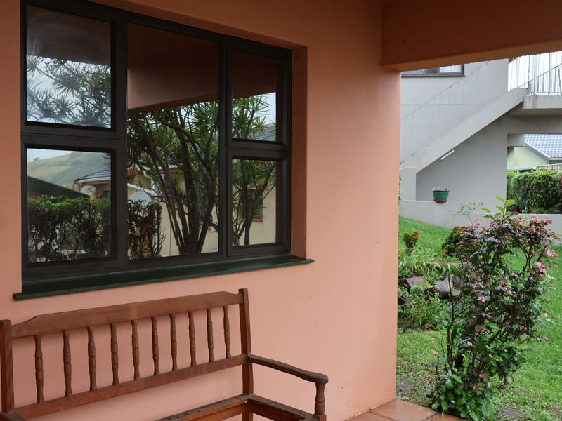 A covered patio area featuring tiled flooring and dark aluminium window frames, overlooking a landscaped garden space.