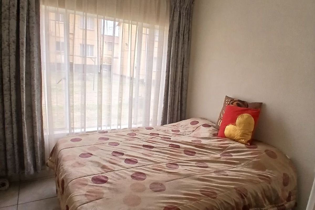 A bedroom featuring tiled flooring and a large window with curtain rails, providing natural light.