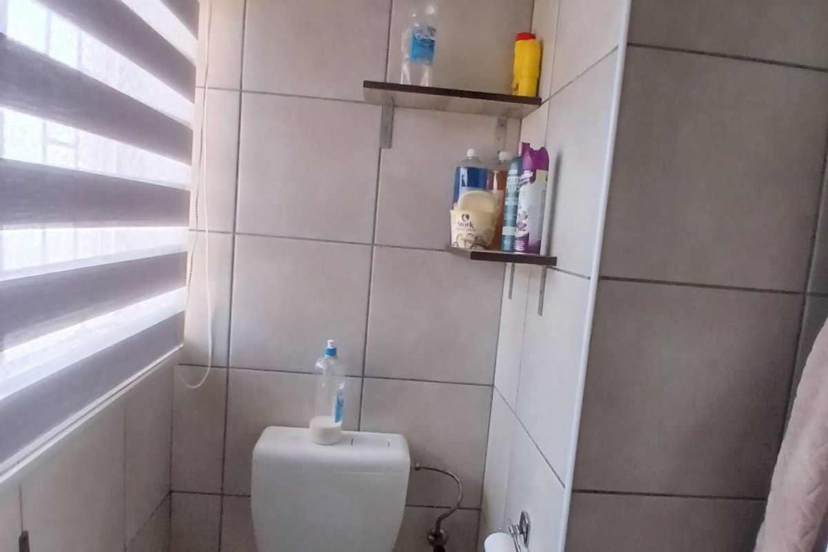 A functional bathroom featuring neutral ceramic wall tiles, a standard toilet, and convenient wall-mounted shelving for storage.