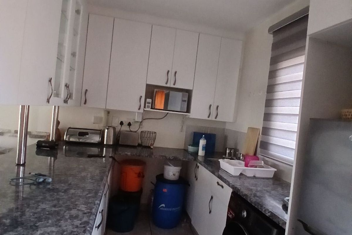 A functional kitchen featuring white cabinetry, granite-look laminate countertops, ceramic floor tiles, and an integrated washing machine.
