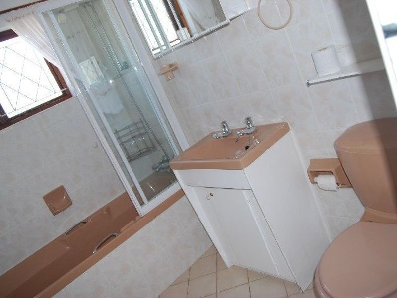 A dated bathroom featuring a peach-colored suite, including a bathtub, toilet, and vanity, with tiled walls and flooring.
