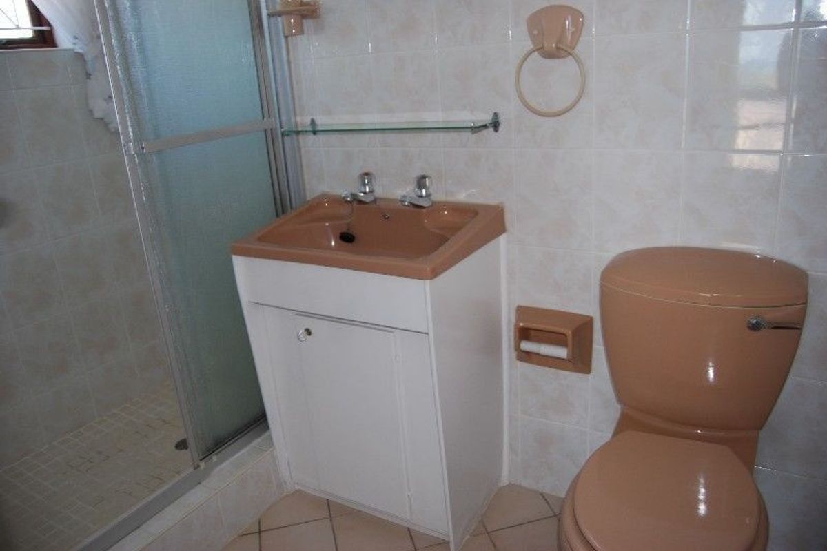 A compact bathroom featuring a shower enclosure, vanity basin, and toilet with dated beige sanitaryware and neutral wall tiling.