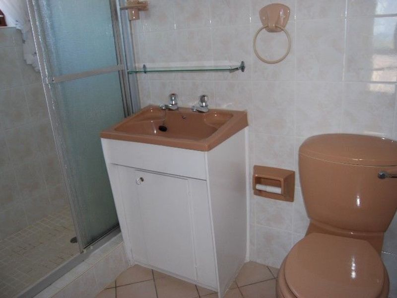 A compact bathroom featuring a shower enclosure, vanity basin, and toilet with dated beige sanitaryware and neutral wall tiling.