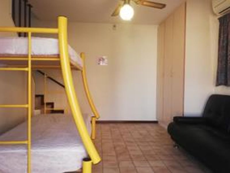 A bedroom featuring tiled flooring, built-in cupboards, a ceiling fan, and an air conditioning unit, with an internal staircase visible.