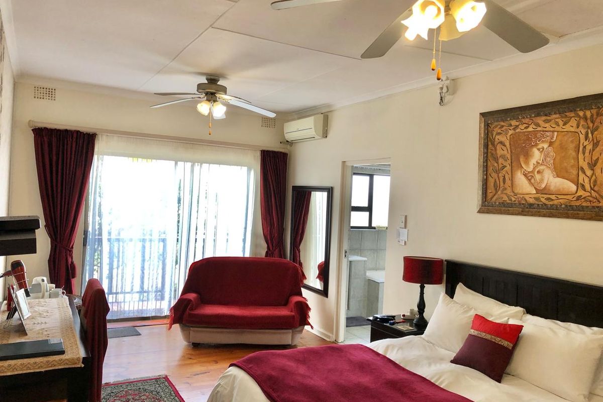 Spacious bedroom featuring hardwood flooring, dual ceiling fans, split-system air conditioning, and direct access to a private balcony and en-suite bathroom.