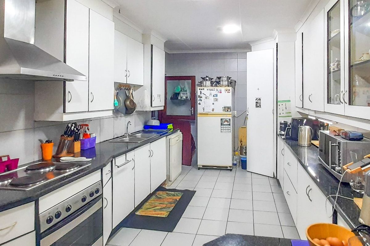 A functional galley-style kitchen featuring white cabinetry, dark granite countertops, tiled flooring, and a stainless steel extractor fan.
